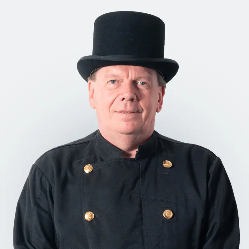 Ein Mann in einer schwarzen Jacke mit goldenen Knöpfen und einem Zylinderhut steht vor einem einfarbigen Hintergrund.